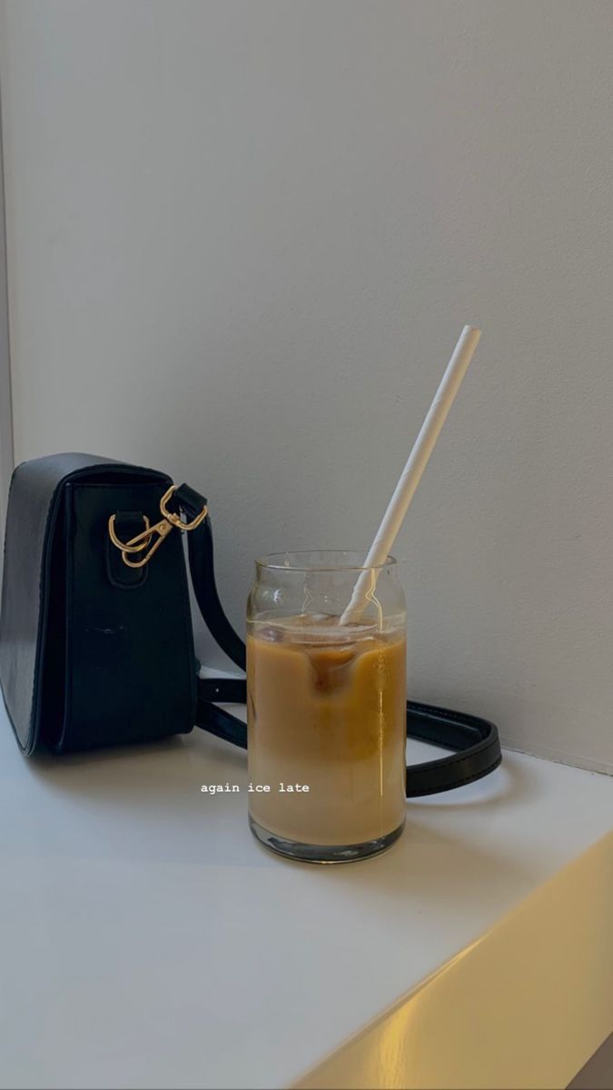 a small black purse sitting on top of a table next to a cup with a straw in it