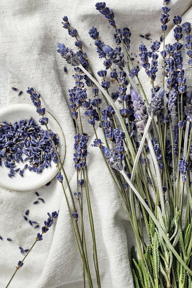 dried lavenders in a white bowl and plate on a linen tablecloth next to the flowers