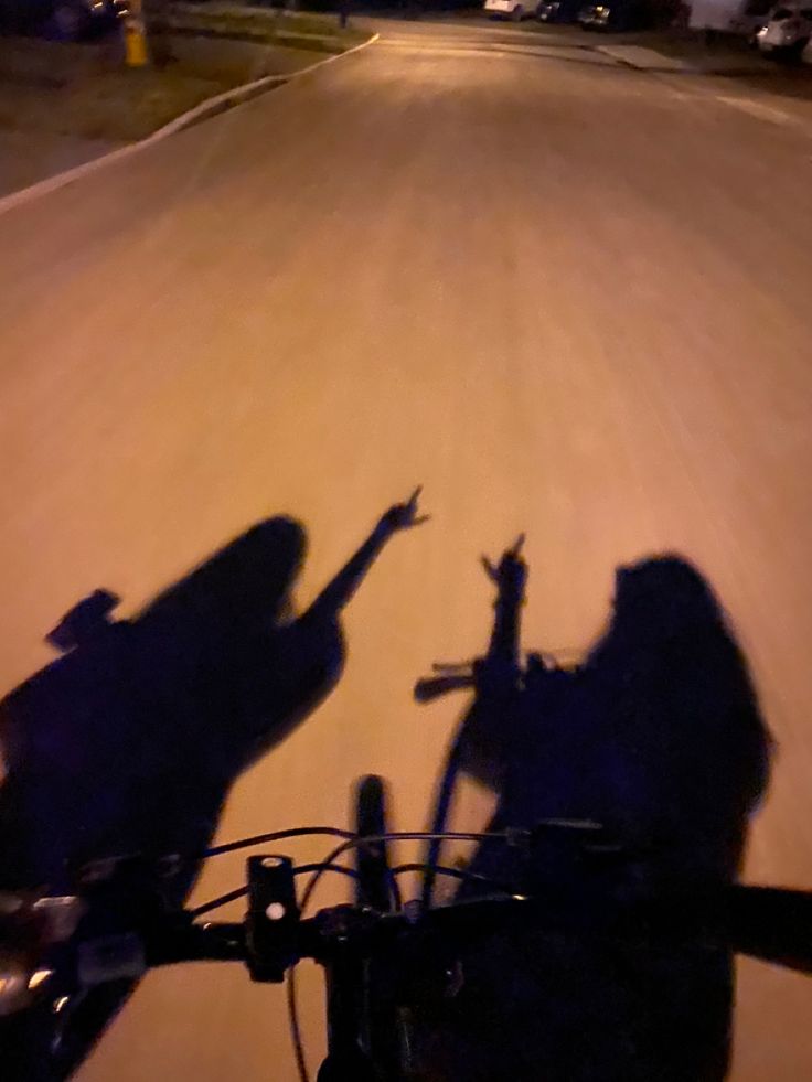 the shadow of two people on a bike riding down a street at night with their hands in the air