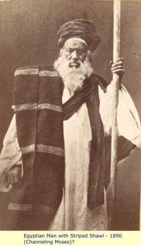 an old man with a long beard holding a stick and wearing a striped shawl