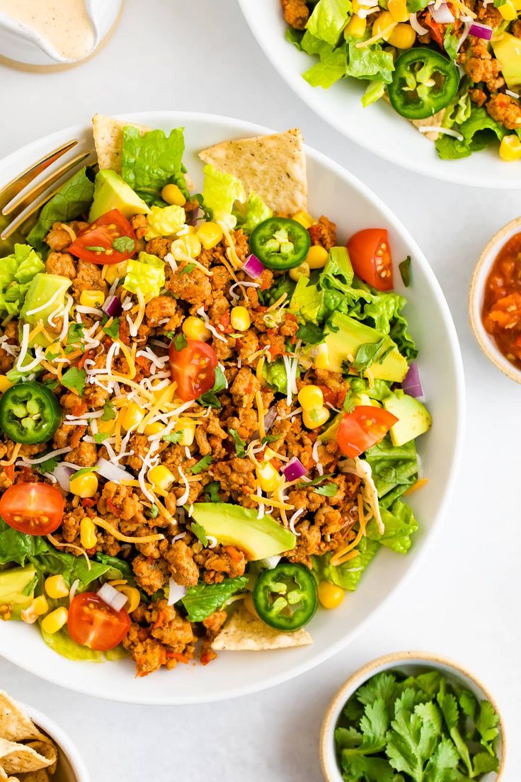 two bowls filled with taco salad next to tortilla chips and salsa sauce