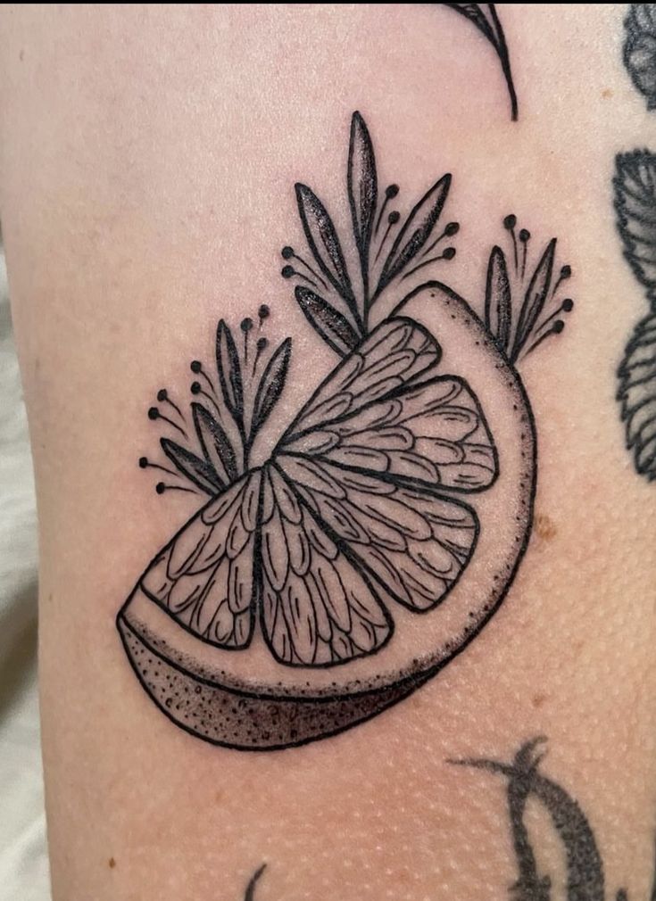 a black and white photo of a piece of fruit on someone's leg with tattoos