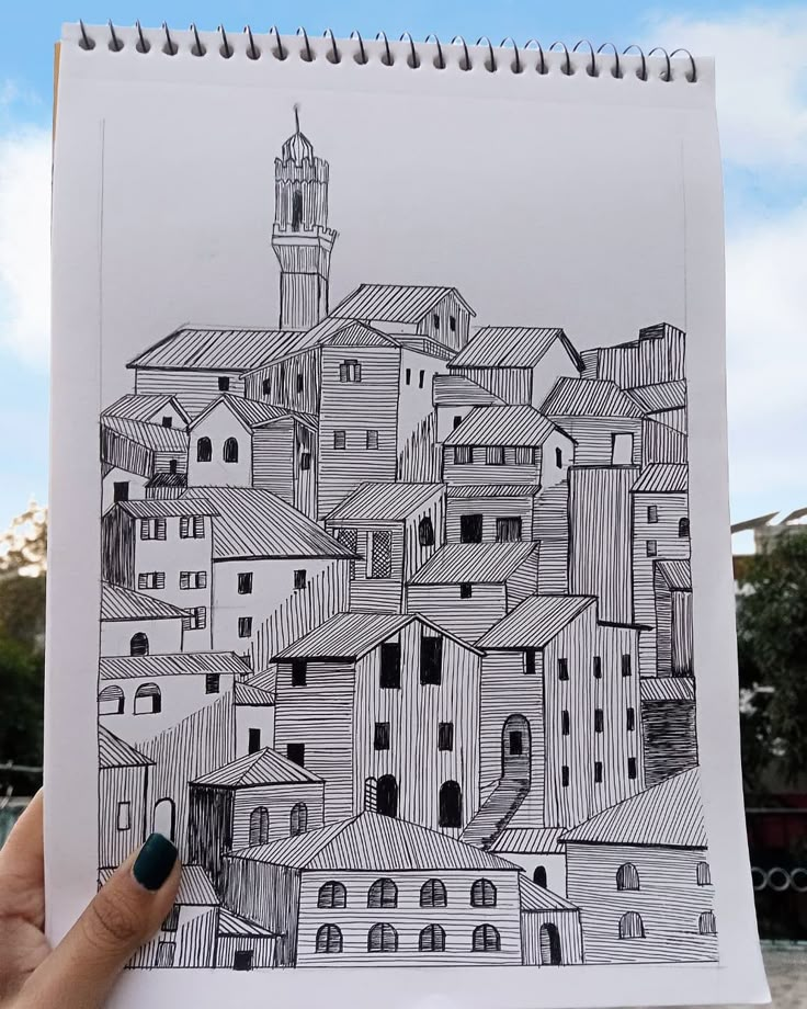 a hand holding up a drawing of a city with buildings and a clock tower in the background