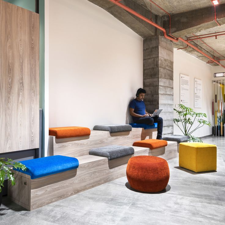 a person sitting on a bench in an office with multiple colored benches and stools