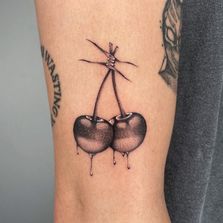 two black cherries hanging from a string tattoo on the right side of the arm