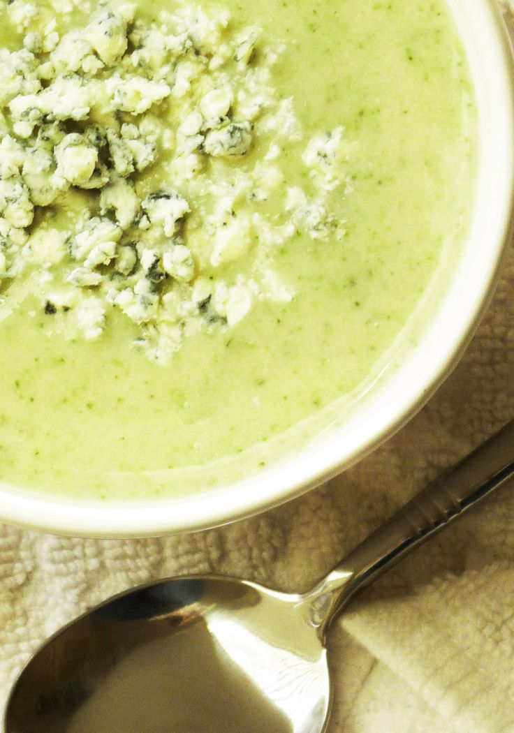 a white bowl filled with broccoli soup on top of a table next to a spoon