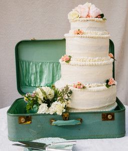 a wedding cake sitting in an open suitcase on a table with flowers and greenery