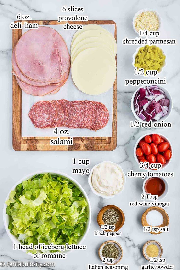 the ingredients for an italian salad laid out on a cutting board, including meat, cheese, lettuce and tomatoes