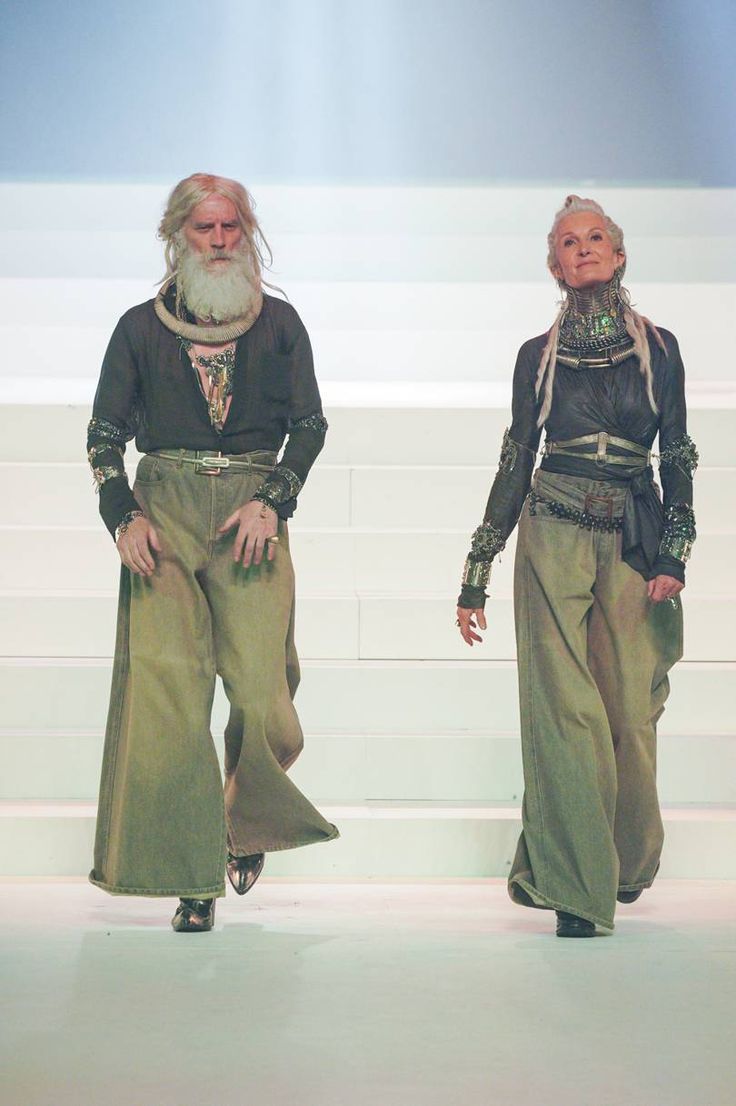 two men with long white hair and beards walking down a runway wearing green pants