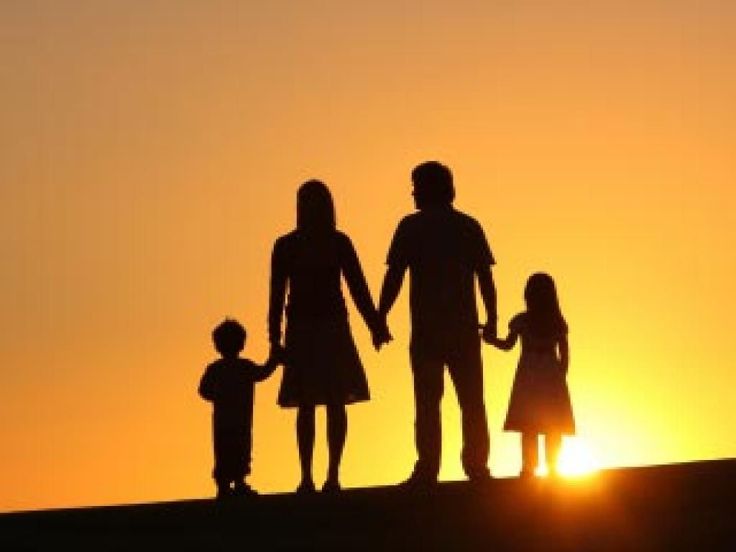 a family silhouetted against an orange sky at sunset with the sun setting behind them