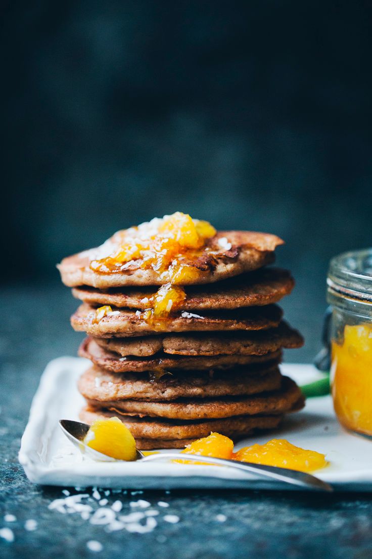 a stack of pancakes sitting on top of a white plate next to a jar of oranges