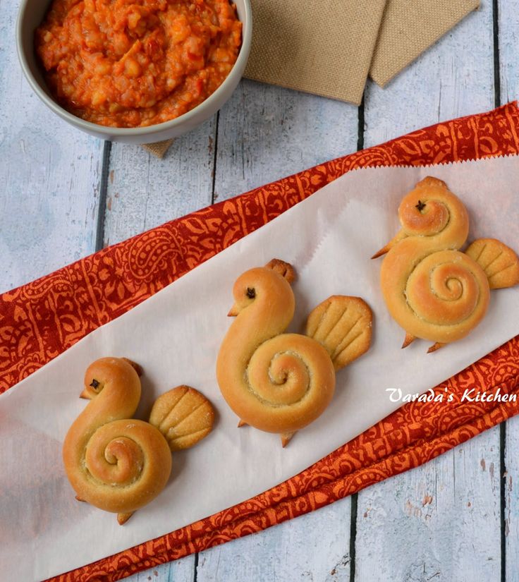 three cookies shaped like snails sitting on top of a paper towel next to a bowl of red sauce