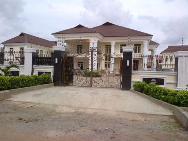 a large white house with a gate in front of it and bushes around the entrance