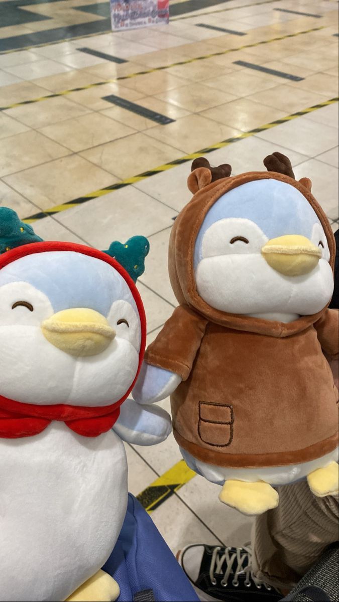 two stuffed penguins are standing next to each other on the floor in an airport lobby