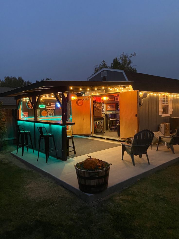 an outdoor bar is lit up at night with lights on the roof and chairs around it