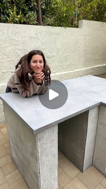 a woman sitting at a concrete bench with her hands on her chin and looking into the camera