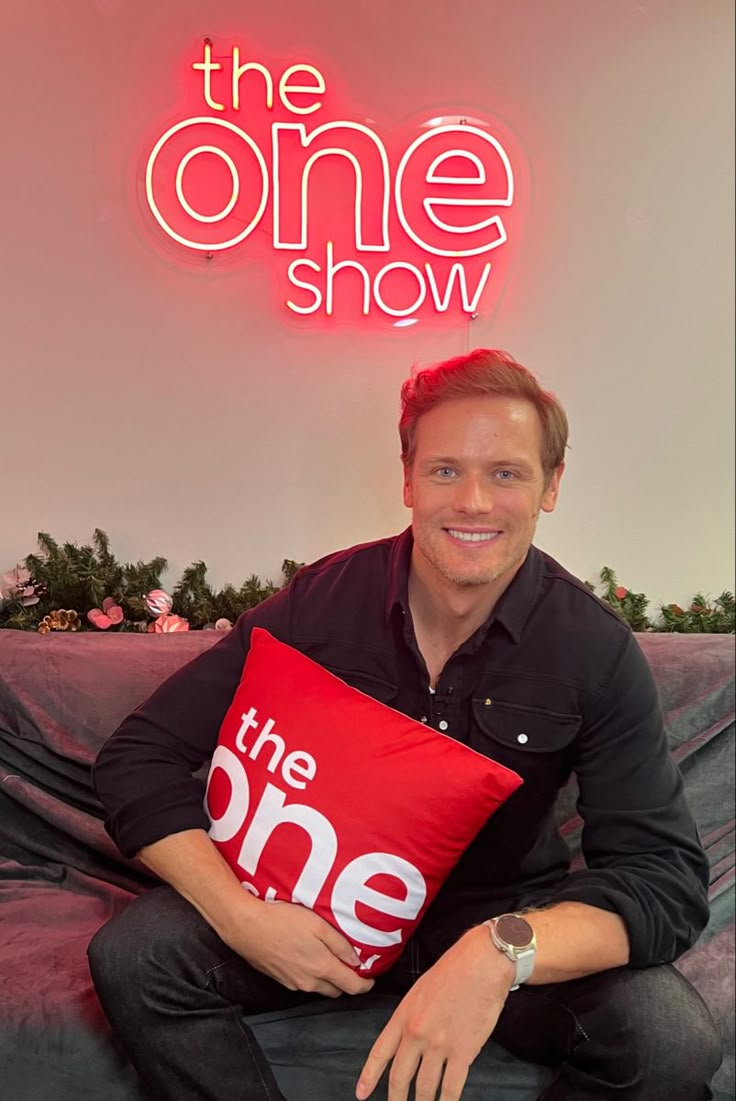 a man sitting on top of a couch holding a pillow in front of a neon sign