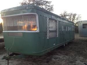 an old green trailer parked in a field next to other trailers and trees at sunset