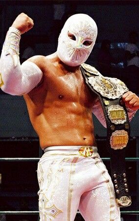 the wrestler is holding his arm up while standing in front of an audience wearing white and gold