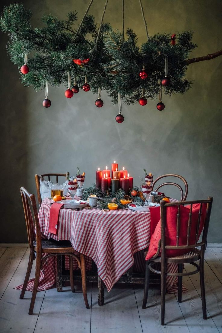 a dining room table with candles and ornaments hanging from the ceiling above it, surrounded by christmas decorations