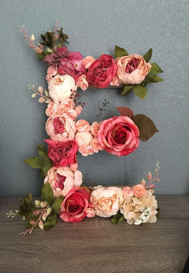 the letter e is made up of flowers and leaves on top of a wooden table