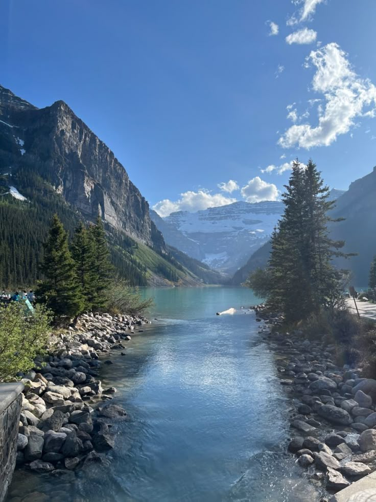 a river running through a lush green forest next to a mountain side covered in snow