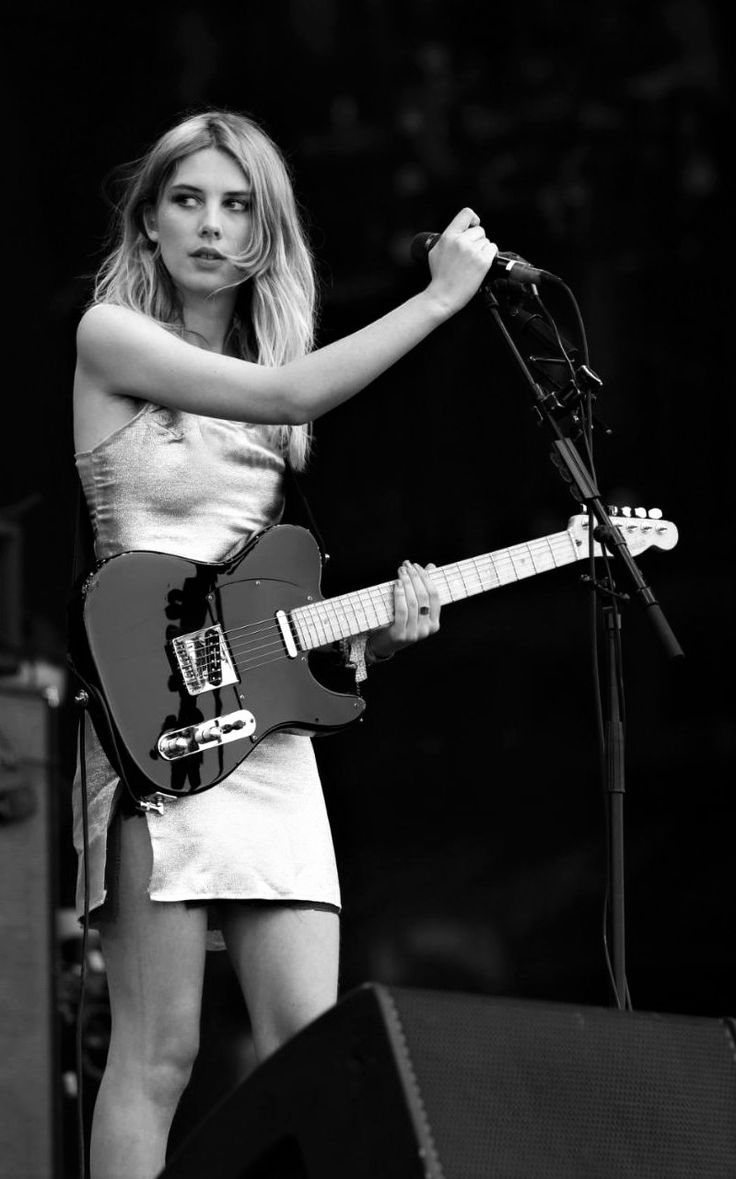 a woman standing next to a microphone holding a guitar