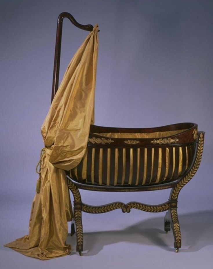 an antique baby crib with gold cloth draped over it's head and legs