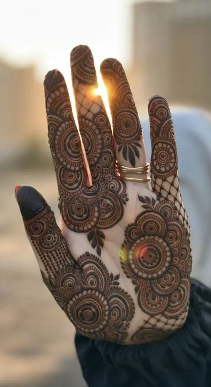 a woman's hand with henna on it and the sun shining through her fingers