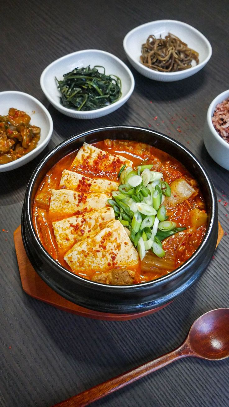 several bowls of food on a table with spoons and chopsticks next to them