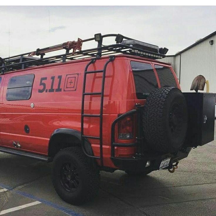 a red van parked in a parking lot next to a building with a ladder on the roof