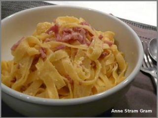 a white bowl filled with pasta and ham on top of a table next to silverware