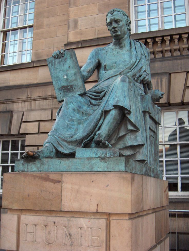 a statue of a man with a book on his lap in front of a building