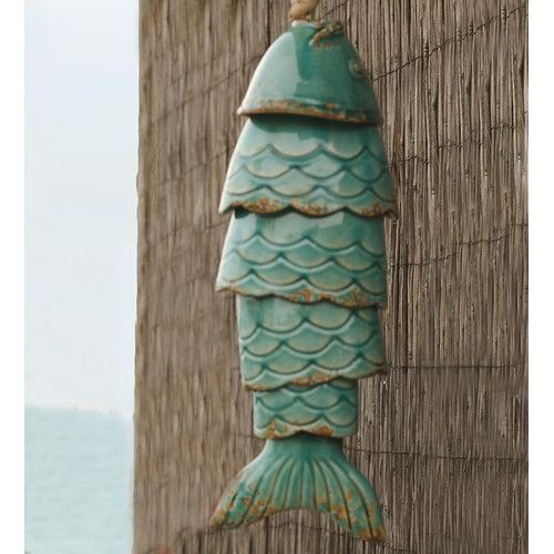 a green fish statue hanging from the side of a wooden building next to the ocean