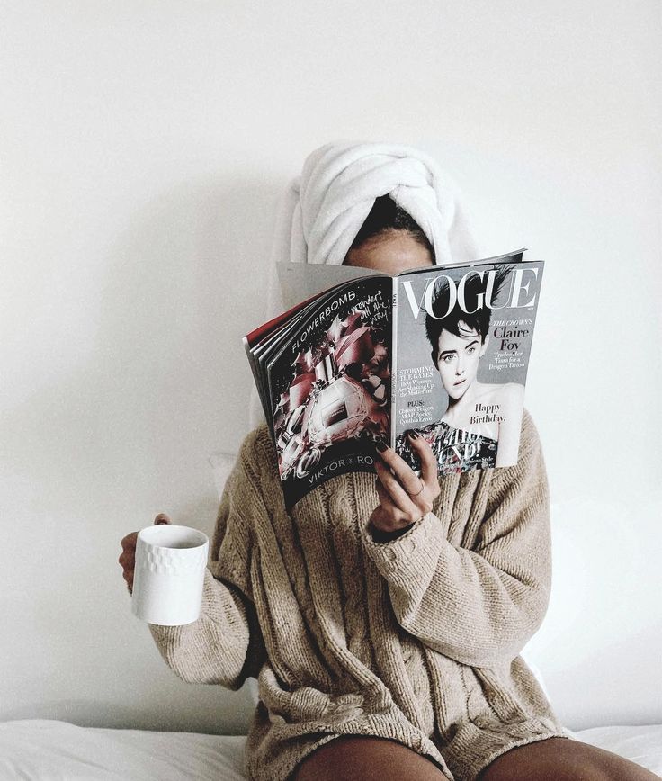 a person sitting on a bed with a towel over their head and reading a magazine