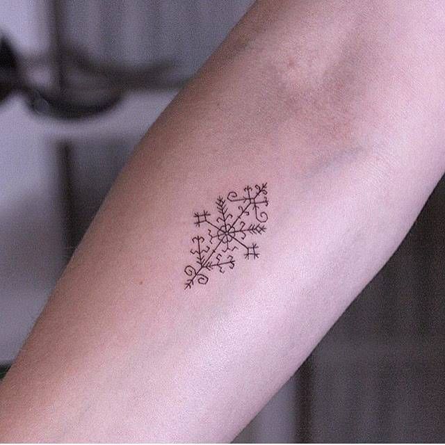 a woman's arm with a small snowflake tattoo on it