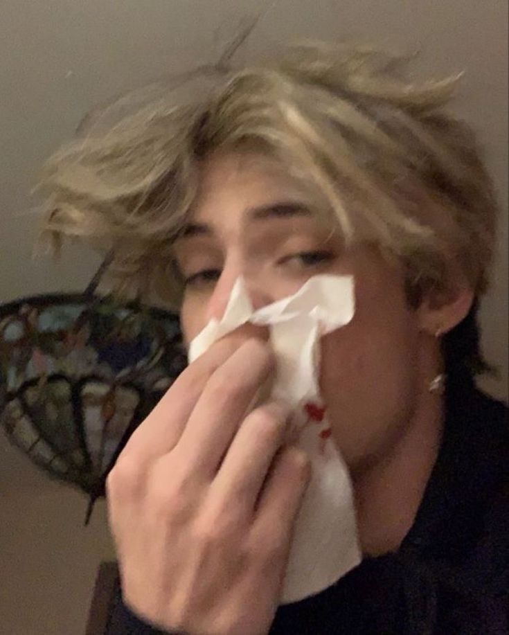 a man with blonde hair is blowing his nose while holding a napkin to his mouth