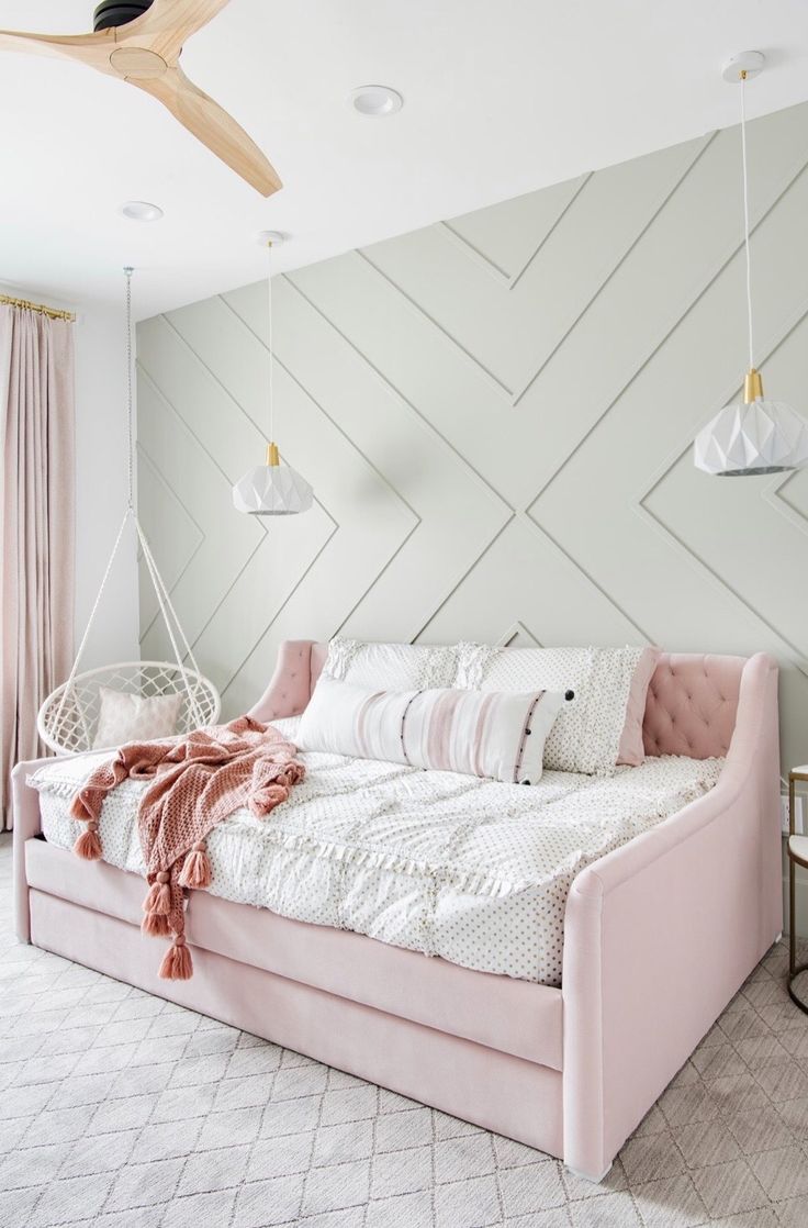 a pink daybed with pillows and blankets on it in front of a white wall