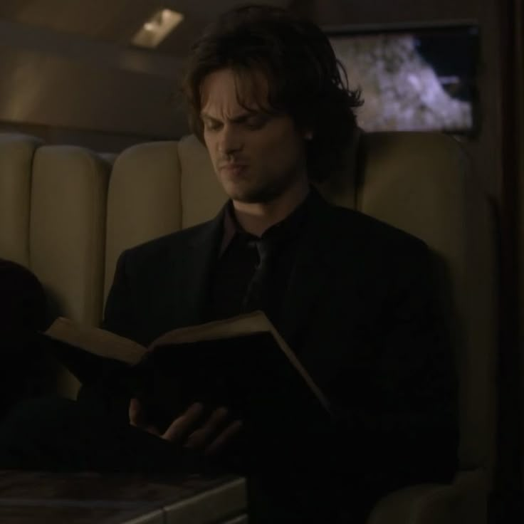 a man reading a book while sitting in a chair on a train or plane at night