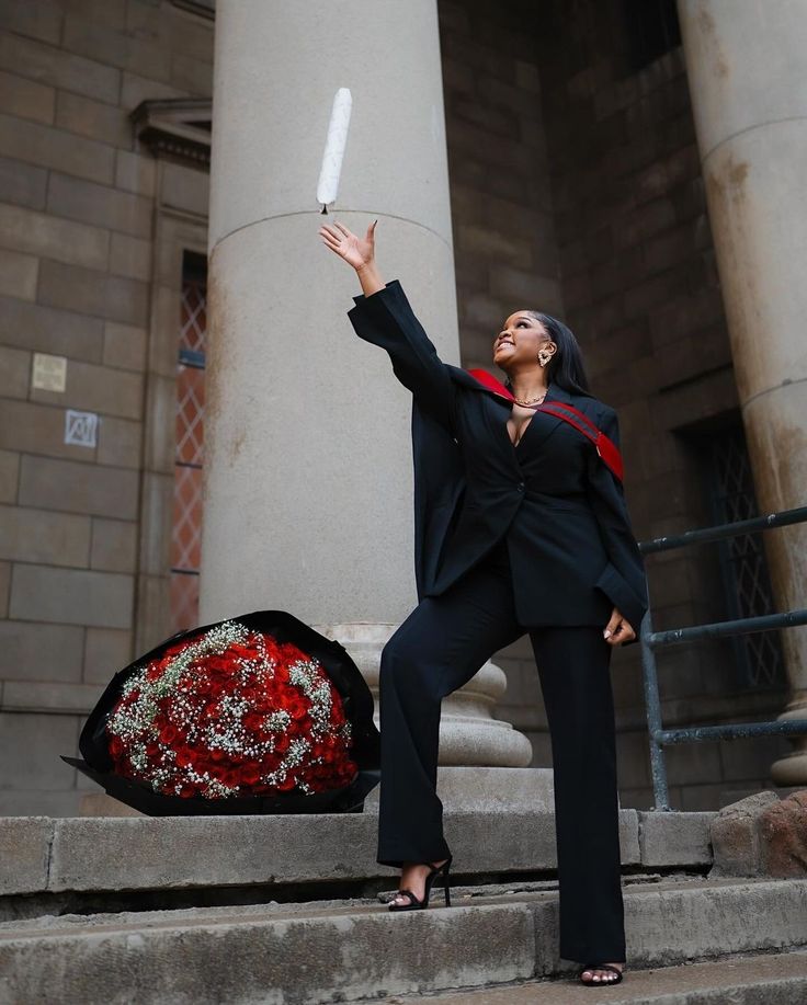 a woman in black suit and red scarf holding up a white object with her right hand