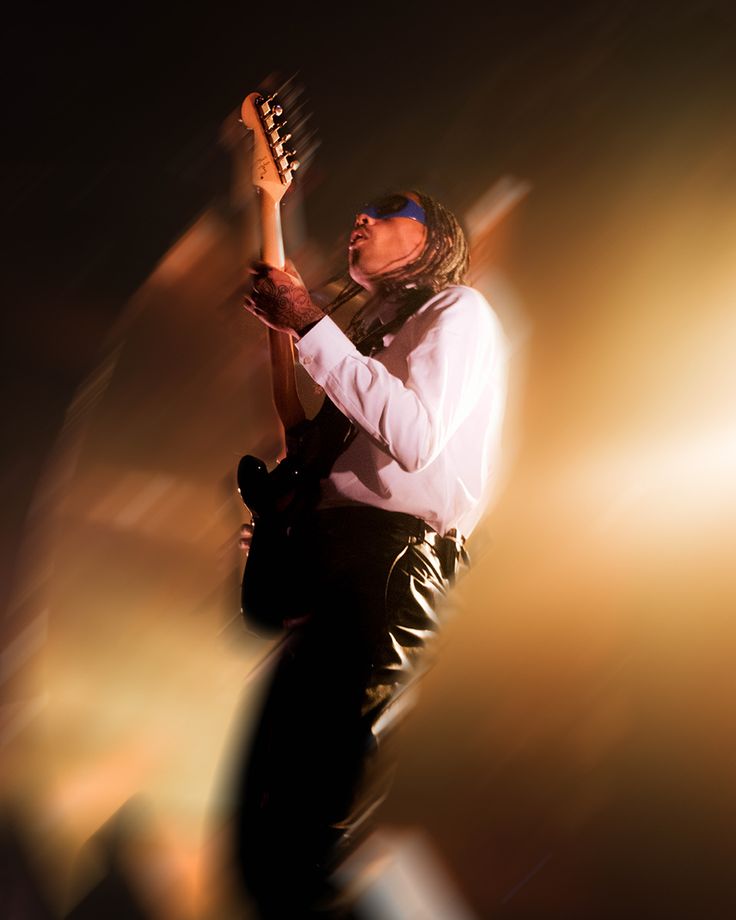 a man holding a guitar in his right hand and looking up at the sky with bright lights behind him