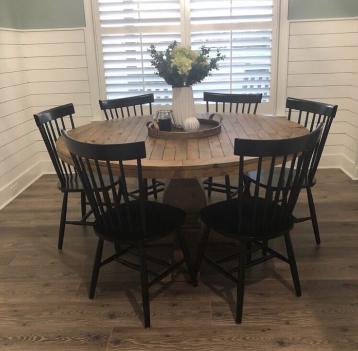 a wooden table with chairs around it in front of a window covered by shutters