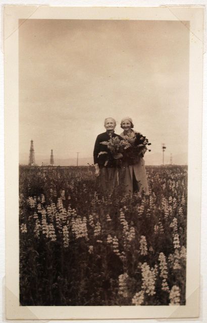 an old black and white photo of two people standing in a field with wildflowers