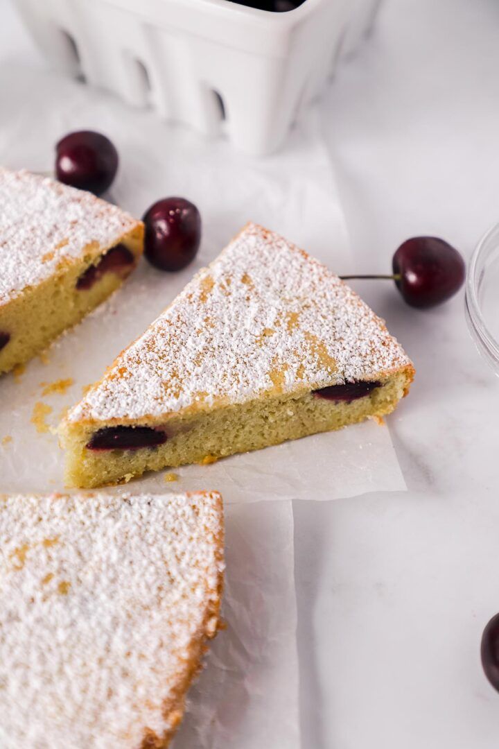 two pieces of cake with powdered sugar and cherries on the table next to it