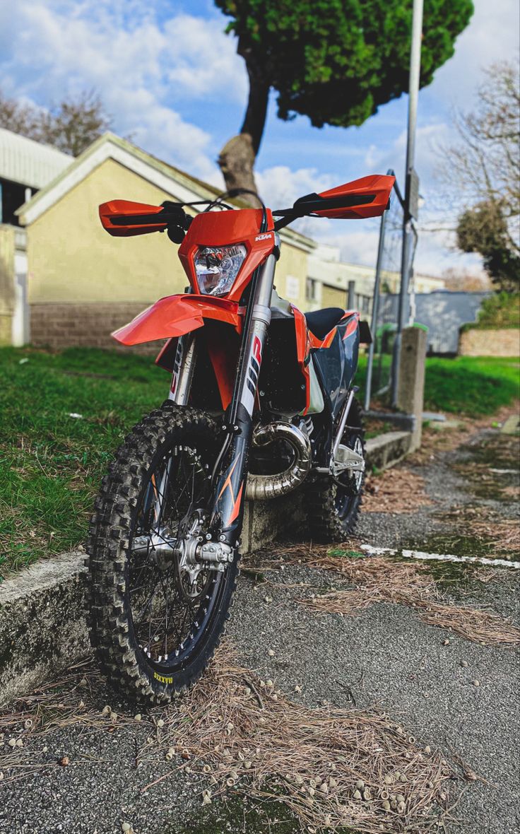 a red dirt bike parked on the side of a road next to a tree and house