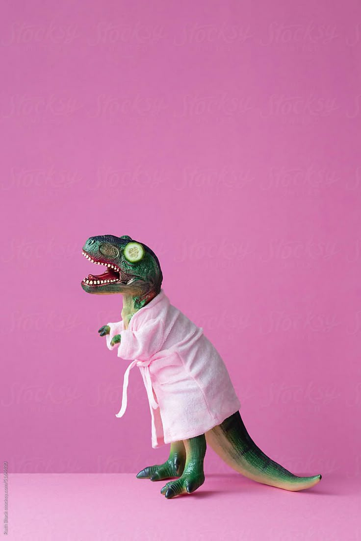 a toy dinosaur wearing a robe with its mouth open and tongue out, on a pink background