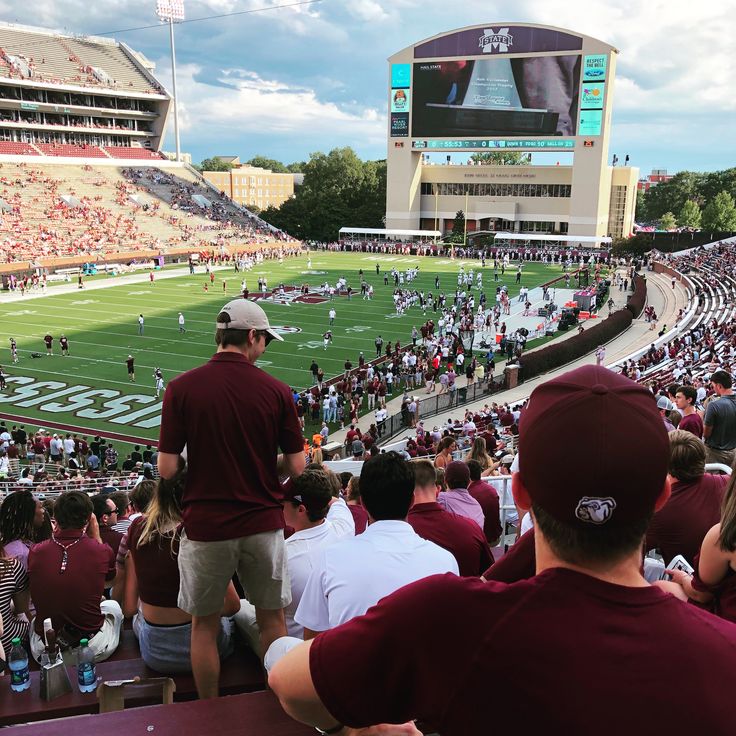 a group of people sitting on top of a football field next to a stadium filled with fans