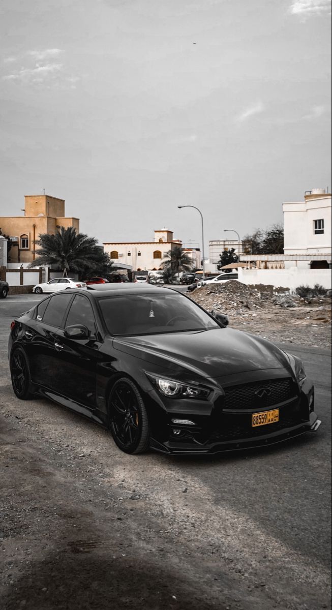 a black car parked on the side of a road next to a parking lot with buildings in the background