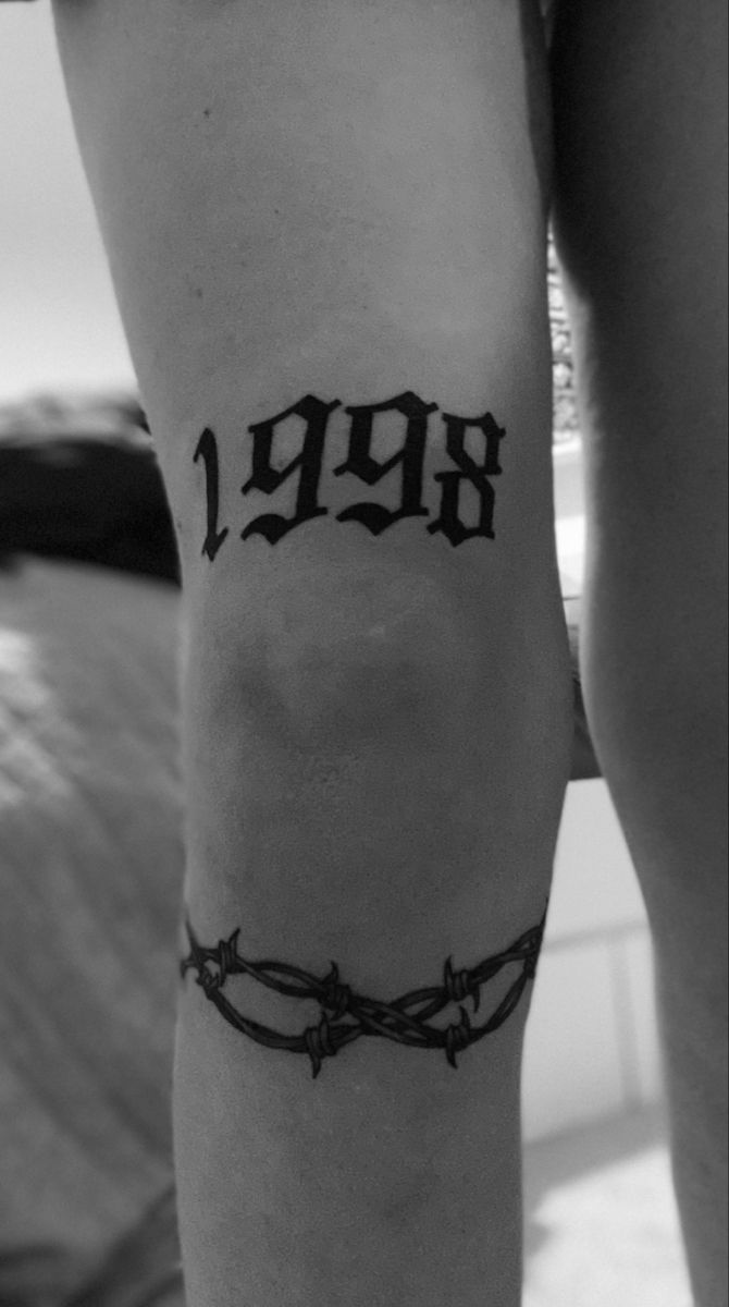 a woman's leg with barbed wire and the word 1989 tattooed on her arm