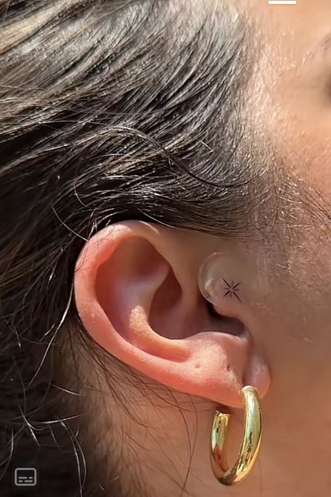 a woman with a small star tattoo on her left side of the ear is wearing a pair of gold hoop earrings